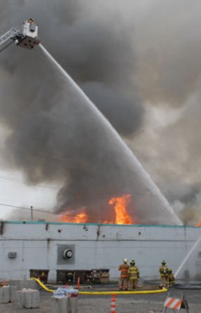 Firefighter in a "bucket" at the end of the extendable ladder attached to a fire truck as he douses a fire in water from a canon